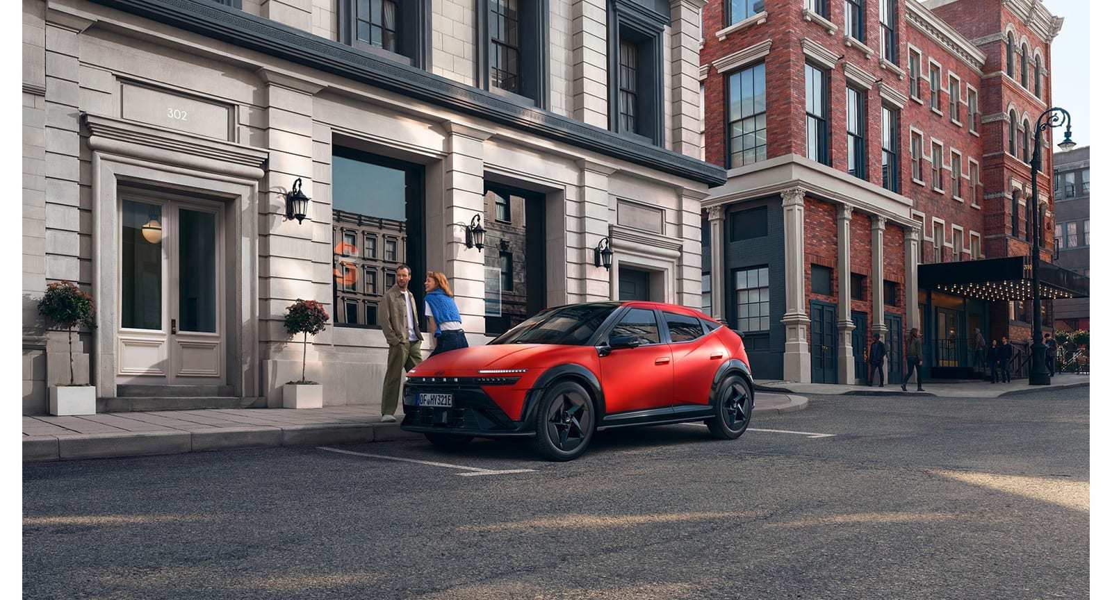 Paar neben dem roten Hyundai IONIQ 3 am Straßenrand vor einem Stadthaus
