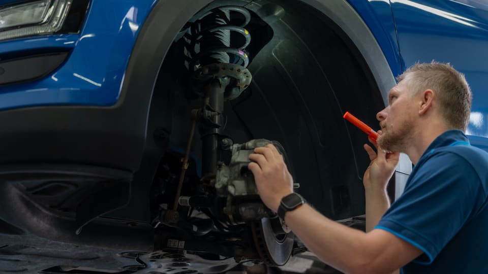 Mechaniker im Hyundai-Polo prüft mit der Taschenlampe die Bremse am Vorderrad