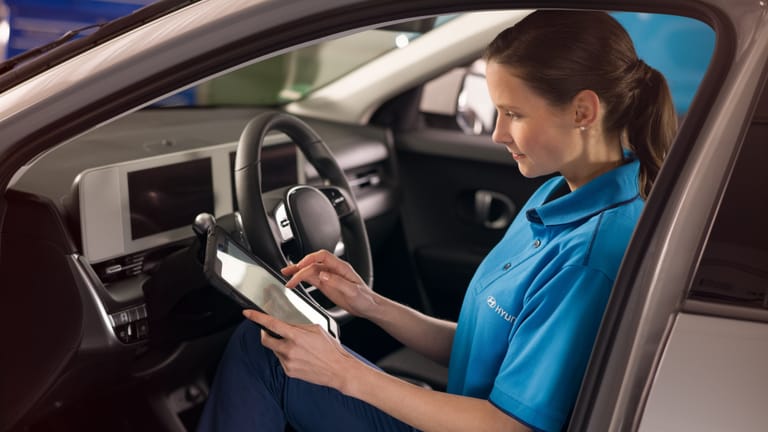 Eine Technikerin sitzt mit einem Diagnosegerät auf dem Fahrersitz und liest die Fahrzeugdaten aus.